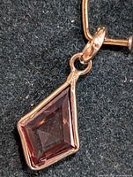 Close-up image of pendant showing kite-shaped, reddish-brown faceted lab-created diamond set in 10K gold bezel.