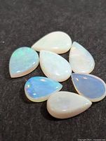 Seven pear-shaped genuine Australian opal cabochons arranged on a dark background showing play of color.
