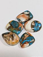 Top view showing five polished multi-colored gemstones with blue, white, brown, and orange hues in varied shapes and smooth finishes.