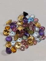 Loose polished faceted gemstones of various colors and shapes on a plain surface.