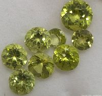 Close-up photo showing eight round faceted light green peridot gemstones with visible facet reflections.