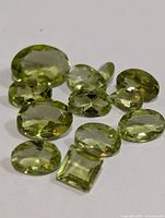 Twelve genuine peridot gemstones arranged on a white background showing various cuts and sizes.