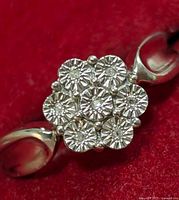 Close-up of the top of the silver ring showing seven diamonds arranged in a floral cluster design with prong settings, polished silver band visible.