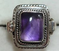 Top view of a sterling silver ring with rectangular amethyst cabochon stone set in engraved bezel.