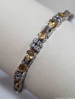 Close-up of sterling silver bracelet displaying pear-shaped yellow citrine and round cubic zirconia stones linked by detailed silver segments.