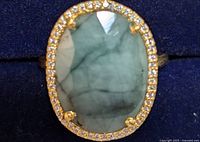 Close-up photo of oval emerald gemstone ring with surrounding small clear stones from top view in dark background