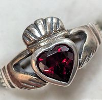 Close-up of the silver Claddagh ring featuring a heart-shaped garnet gemstone, showing the detailed design of the hands and crown around the stone.