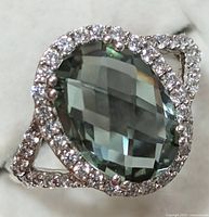 Close-up of top of silver ring with large oval faceted green amethyst surrounded by clear stones.