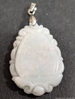Front view of the white jadeite pendant showing smooth carved design and silver bail on a black background.