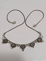 View of the full necklace laid flat, showing the silver chain, curved bar, decorative silver filigree and five bezel-set moonstone cabochons along the bar.