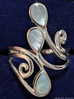 Close-up front view of the silver ring with three pear-shaped mother of pearl pieces set in an ornamental style with curls and swirls in the band.