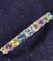 Close-up of ring showing multi colored gemstones in silver band from angled view