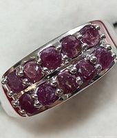 Close-up angled photo showing rows of raw ruby stones set in silver ring.
