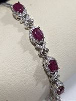 Close-up side angle of the silver bracelet showing ruby and cubic zirconia stones on a cream background.