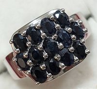 Close-up front view of silver ring showing rectangular cluster of dark blue faceted sapphire stones set with prongs.