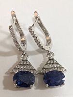 Front view of the pair of silver earrings showing oval blue sapphire stones and triangular cubic zirconia accents.