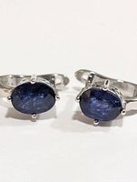 Front view of pair of silver cufflinks each featuring an oval dark blue sapphire stone in claw setting