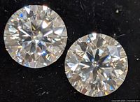 Two round brilliant moissanite stones laid side-by-side, showing clarity and sparkle on black background.