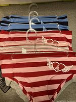 Front view of the 10 pairs of ladies boycut panties in various striped colors including blue, pink, and red, hanging on clear plastic hangers.