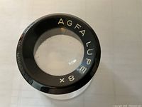 Top view of black-framed Agfa Lupe 8x magnifier showing gold lettered brand and magnification on outer ring.