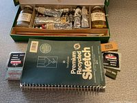 Photo showing oil paint tubes, brushes, sketchbook, erasers, sharpener and artist medium jars