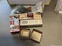 Top view of various art supplies including DAS polymer clay, Reeves sketching paper, Nu Brush brushes and wooden frame on grey fabric surface