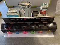 Photo of assorted art paints including fluorescent paint pots, metal tins, tubes, and jars
