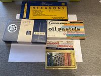 Photo showing box of Hexagon pastels, Grumbacher oil pastels, Reeves pastels, and Stubbi Sticks laquapast crayons