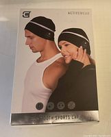 Front view of the product box showing male and female models wearing the black Bluetooth sports caps with reflective stripes on a white background.