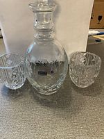 Decanter and two glasses shown together on carpeted floor with a white background.