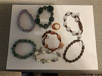 Photo showing six beaded bracelets of various colors and designs along with one orange ring.