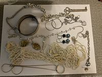 Photo of assorted costume jewelry including various necklaces, earrings, bracelets, and key pendant displayed on a white surface.