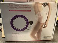 Boxed purple hula hoop with fitness benefits detailed on packaging including tightening waist and hip muscles, exercise waist, increasing leg elasticity, and decreasing waist fat.