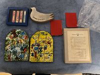 View of all items from above: two stained glass style mezuzahs, ceramic dove, four red velvet cases, informational booklet from Israel Museum, plastic sleeve