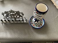 Photo showing metal Hanukkah menorah with lion design next to colorful ceramic cup on patterned plate.