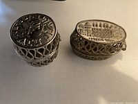 Two silver-tone metal Judaica Shabbat travel candle holders shown from above, displaying embossed tops with Hebrew and Jewish cultural images.