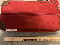 Side view of red suede liquor bottle case with zipper and label 'Picnic at Ascot' next to a ruler showing approximately 15 inches in length.