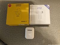 Photo showing two sets of Bluetooth earbuds in boxes: UMIDIGI AirBuds U and i12 TWS, along with a third pair outside boxes.