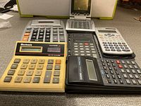Photo showing all seven calculators arranged on a table with various brands and types visible.