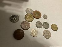 Overview of all 12 assorted coins showing variety in size, shape, and metal finishes arranged flat on white surface.