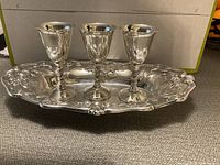 Silverplate oval tray with three matching decorative goblets on top, showing detailed embossing and floral motifs.
