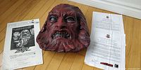 Overview of replica Zardoz mask, certificate papers, and press book on wooden floor