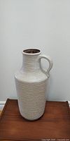 Full frontal view of tall ceramic floor vase with horizontal ribbed texture and handle.
