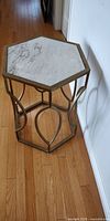 Full view of the hexagonal side table showing the brass-colored metal frame and marble top on a wooden floor.