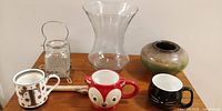Photo of entire lot showing all items together on table: tall clear glass vase, antique condiment server, ceramic candle holder, driftwood piece, and 3 mugs (fox, T and black).