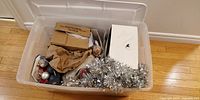 Plastic storage tote's top view showing assorted Christmas decorations packed inside, including silver tinsel and boxed items