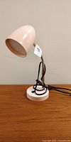 Side view of the pink desk lamp showing the egg-shaped shade, gooseneck arm, round base, and attached black power cord.