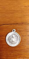 Front side of the vintage religious pendant showing a seated figure with inscription.