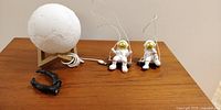 Astronaut swings, moon lamp, and wall hangers displayed on wood surface with charging cord visible.