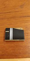 Front view of rectangular vintage Japanese lighter showing black finish with brass trim and silver-tone decorative strip.